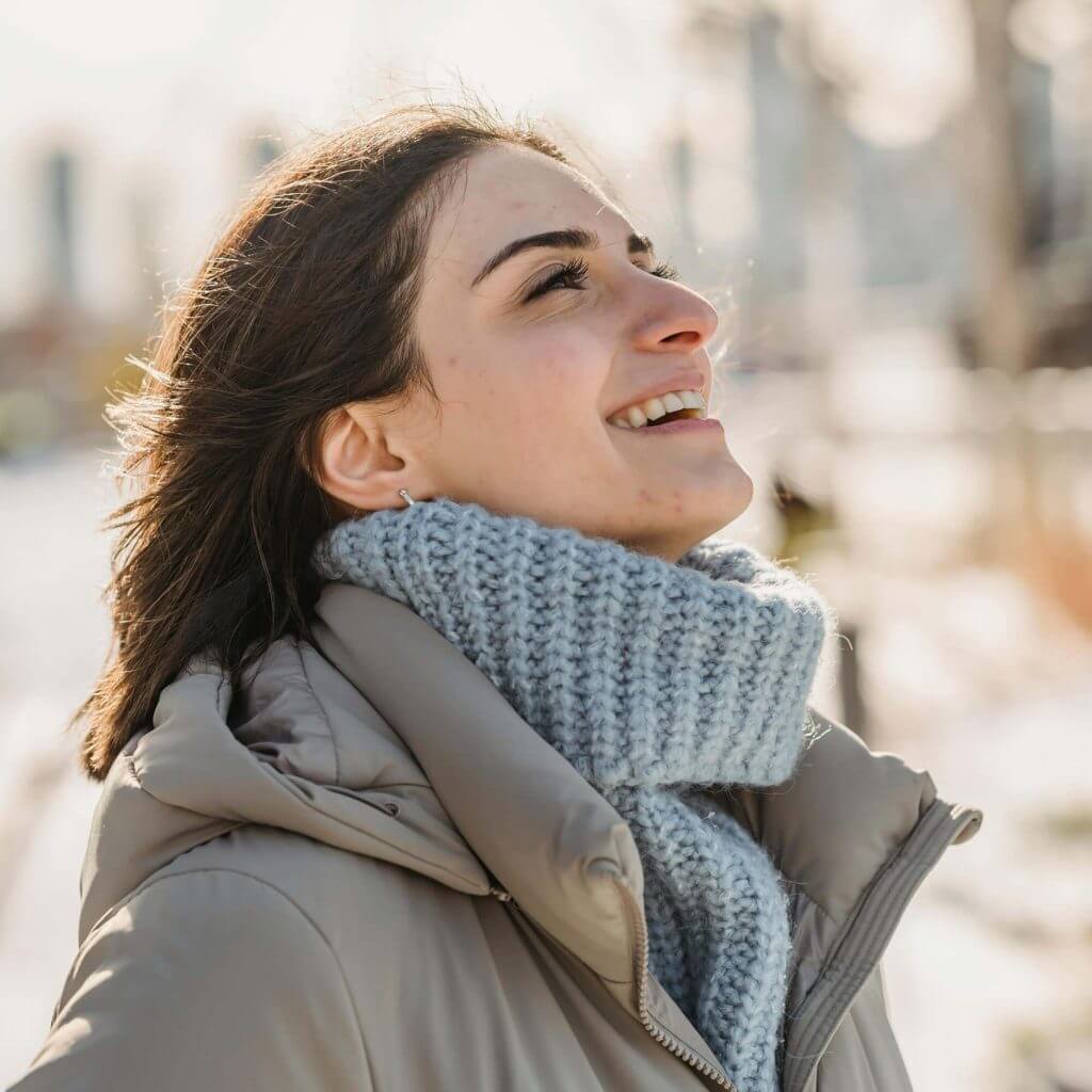 Woman in gray turtleneck and jacket smiling and looking up, symbolizing relief received from The Remedy's personalized mental health care