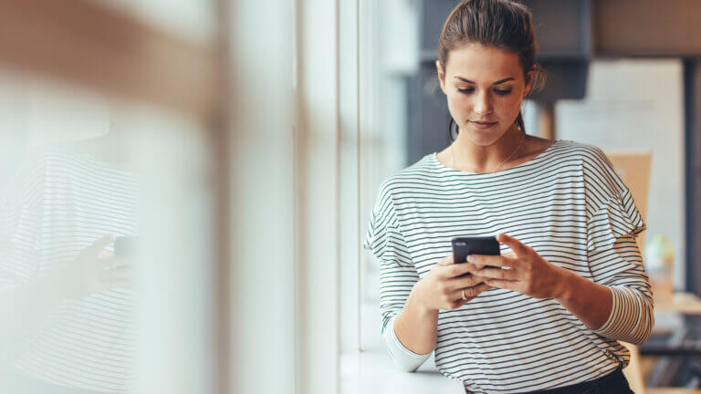 Person in a striped shirt looking at a phone, representing The Remedy's telemental health services and availability to people with busy lifestyles