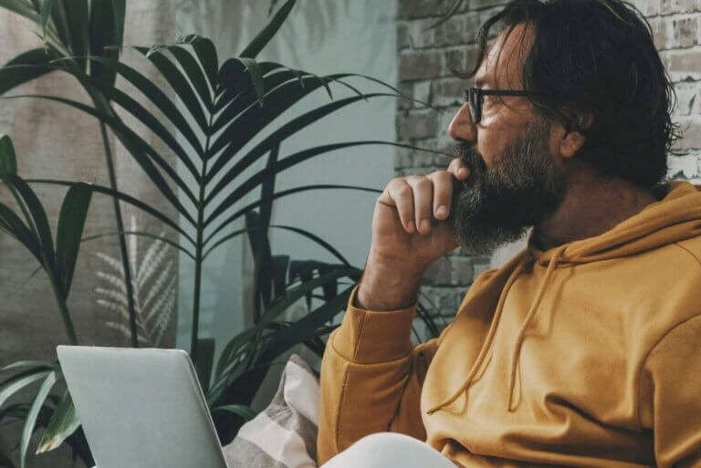 Person in a mustard hoodie and glasses with laptop, appearing contemplative